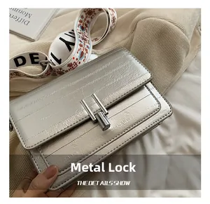 Detail of silver metallic square bag with precision metal lock and embroidered strap