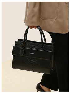 Detailed close-up of a black crocodile pattern handbag with smooth leather panel details