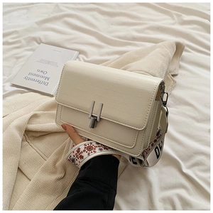 Detail of cream white faux leather bag with textured finish and embroidered wide strap