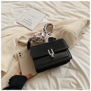 Close-up of black textured crossbody bag with silver buckle and patterned wide strap
