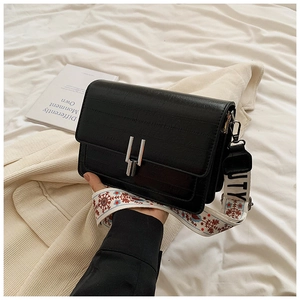 Detail of black embossed leather bag with ethnic style embroidered wide strap and silver buckle