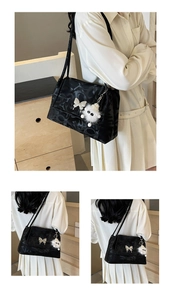 Detail of black tote bag featuring subtle logo pattern and plush doll with butterfly charm
