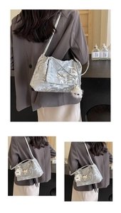 Detail of silver tote bag featuring abstract letters, butterfly buckle and plush charm