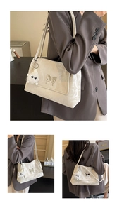 Detail of cream shoulder bag with silver butterfly emblem and plush monster charm