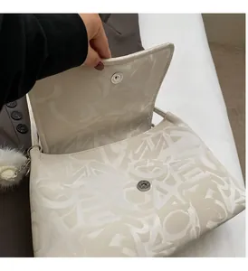 Close-up of cream monogram tote bag with cylindrical magnetic clasp and fur ball charm