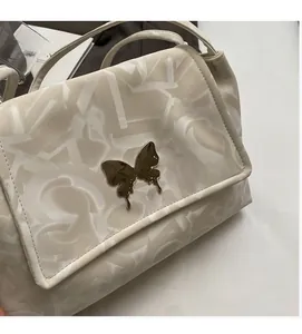 Detail view of cream tote bag featuring printed patterns and a metallic butterfly ornament