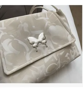 Close-up of silver butterfly metal buckle on cream faux leather textured tote bag