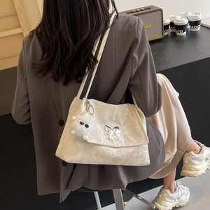 Close-up of off-white tote bag with letter print, butterfly charm and plush pendant