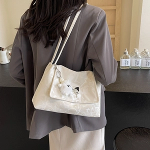 Detailed view of a white jacquard tote bag with a plush puppy charm on a model