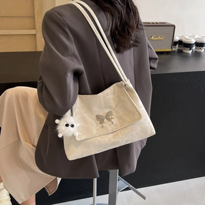 Detail of cream shoulder bag featuring embossed texture and a metal bow ornament