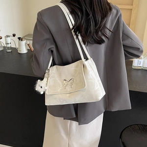 Detail of white tote bag featuring metallic butterfly charm and soft plush keychain accessory