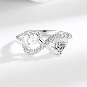 Silver infinity ring with baby footprints and heart stone on a white background