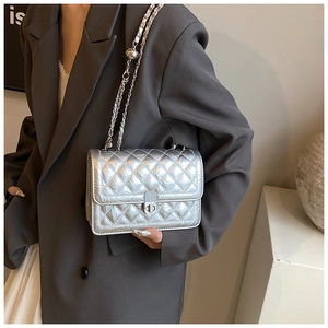 Detail of silver metallic quilted chain bag with twist lock on model in grey suit