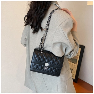 Detail showing the glossy black quilted texture and silver chain strap on a shoulder bag
