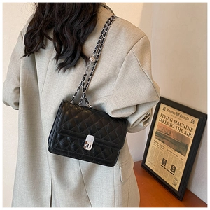 Detail of black quilted leather shoulder bag with silver chain strap and metal swivel lock