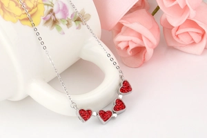 Gros plan d'un pendentif cœur en argent avec cristaux rouges près d'une tasse et d'une rose