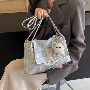 Silver metallic tote bag with abstract texture and plush charm shown on a model