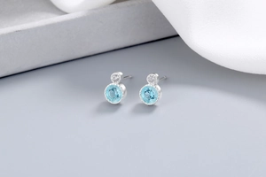Detailed view of silver stud earrings featuring bright blue round gemstones and tiny zircons