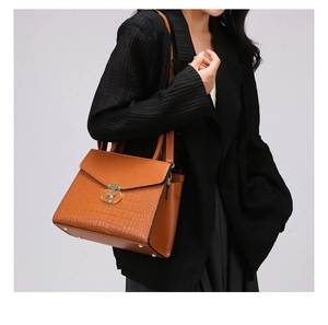 Detail of crocodile embossed brown handbag with golden metal twist lock and shoulder strap