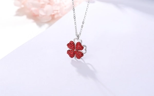 Détail des cristaux cœur rouge pliables sur collier trèfle argenté avec accent floral
