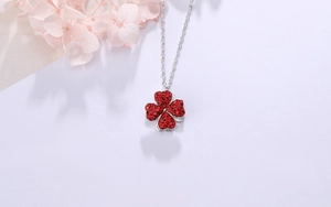 Détail d'un collier chaîne argentée avec un pendentif trèfle à quatre feuilles rouge