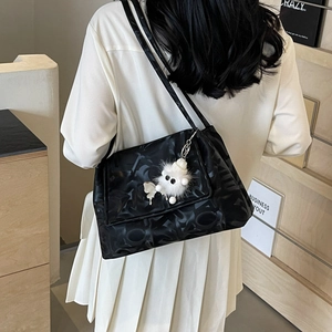 Detail of black tote bag with embossed letter texture and plush monster pendant on strap