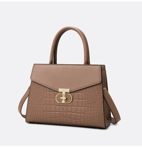 Detail of tan crocodile embossed texture and golden T-shaped metal lock on handbag