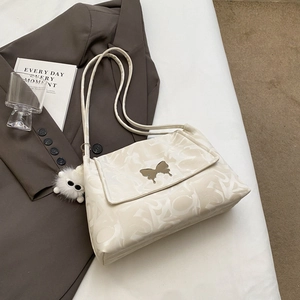 Detail of cream shoulder bag featuring embossed letters and a golden butterfly clasp