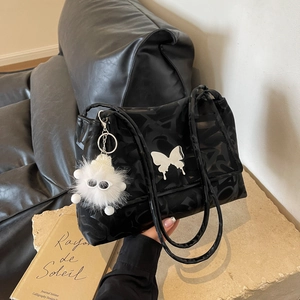 Detail of black tote bag with white butterfly decor and plush charm on stone base