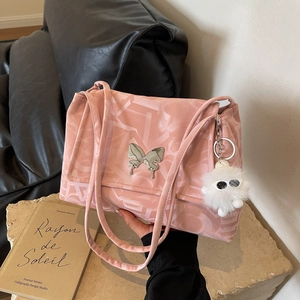 Detail of pink shoulder bag with letter prints, butterfly buckle and plush monster charm