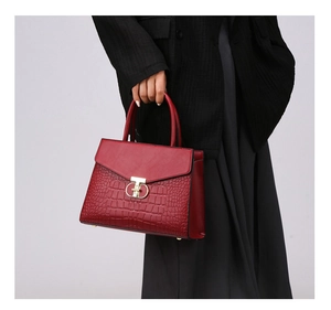 Detail of red croc-effect leather tote bag with gold twist lock held by a model