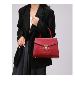 Detail view of red faux crocodile leather handbag with gold twist-lock on suit model