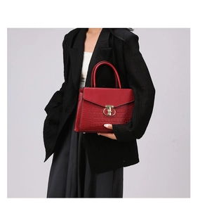Detail of dark red croc-embossed handbag featuring gold twist lock and round handles