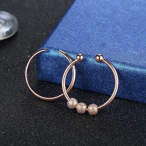 Macro detail of rose gold hoop earrings with three frosted beads on a textured box