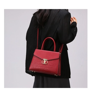 Detail of red faux crocodile leather handbag with golden twist lock and metal feet
