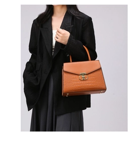 Detail view of brown crocodile texture briefcase handbag with gold clasp on model