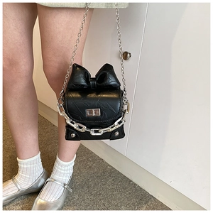 Detail of a black bow-tie crossbody box bag with silver chains on a model