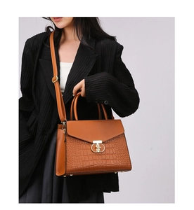 Detail shot of brown crocodile pattern leather handbag with gold buckle and adjustable strap