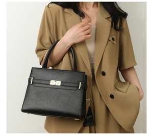 Détail d'un sac à main noir en cuir grainé avec fermoir doré porté par le mannequin