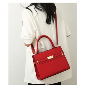 Vue détaillée du sac à main rouge en cuir grainé avec fermoir doré sur manteau blanc