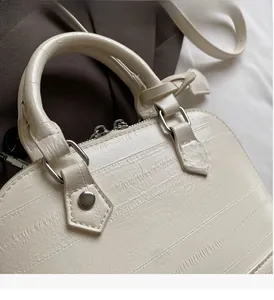 Detail of cream-white shell bag showing textured leather finish and silver metal hardware