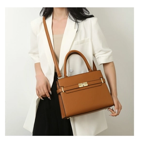 Sac à main marron en cuir avec fermoir rotatif porté par un mannequin en blazer blanc