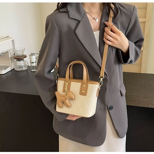 Détail du sac seau matelassé crème avec charm chien marron porté sur une veste grise