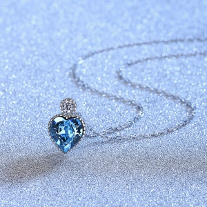 Silver plated heart necklace with blue crystal pendant on a sparkling blue background