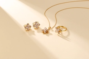 Flat lay of gold flower jewelry set with sparkling zircon petals on beige surface