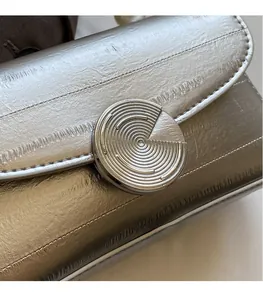 Détail d'un sac à rabat métallisé avec boucle en métal 3D et cuir texturé plissé