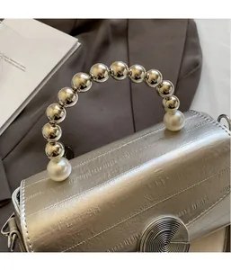 Détail du sac à main argenté avec poignée en perles et fermoir métallique texturé