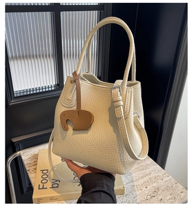 Detail of lychee textured leather bucket bag with cute brown elephant charm on marble top
