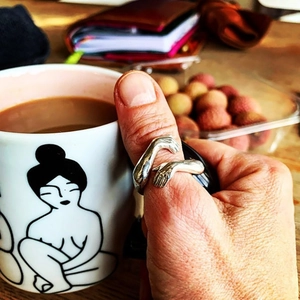 Detailed view of silver hugging hands open ring worn while holding a coffee cup