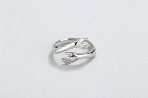 Macro detail of silver hugging hands ring featuring a polished metal finish and open design